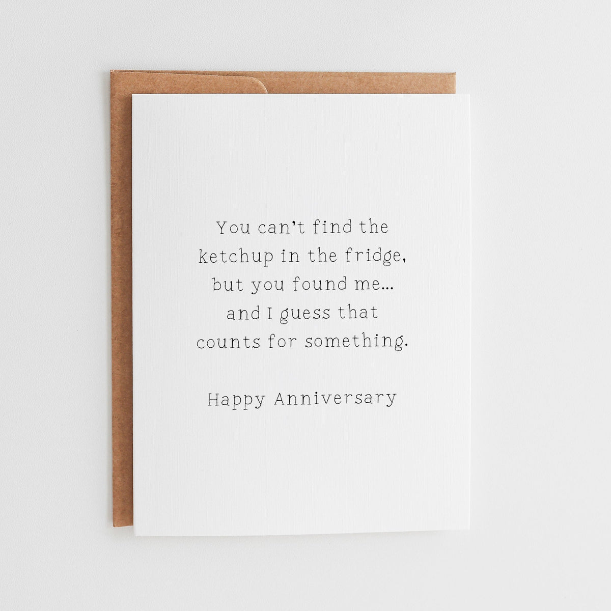 White funny anniversary card about finding love but not the ketchup, displayed with a brown kraft envelope.